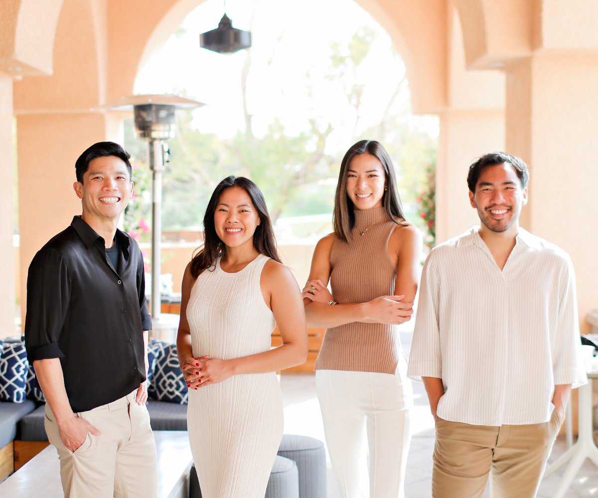 Four smiling colleagues standing together in a bright lounge.