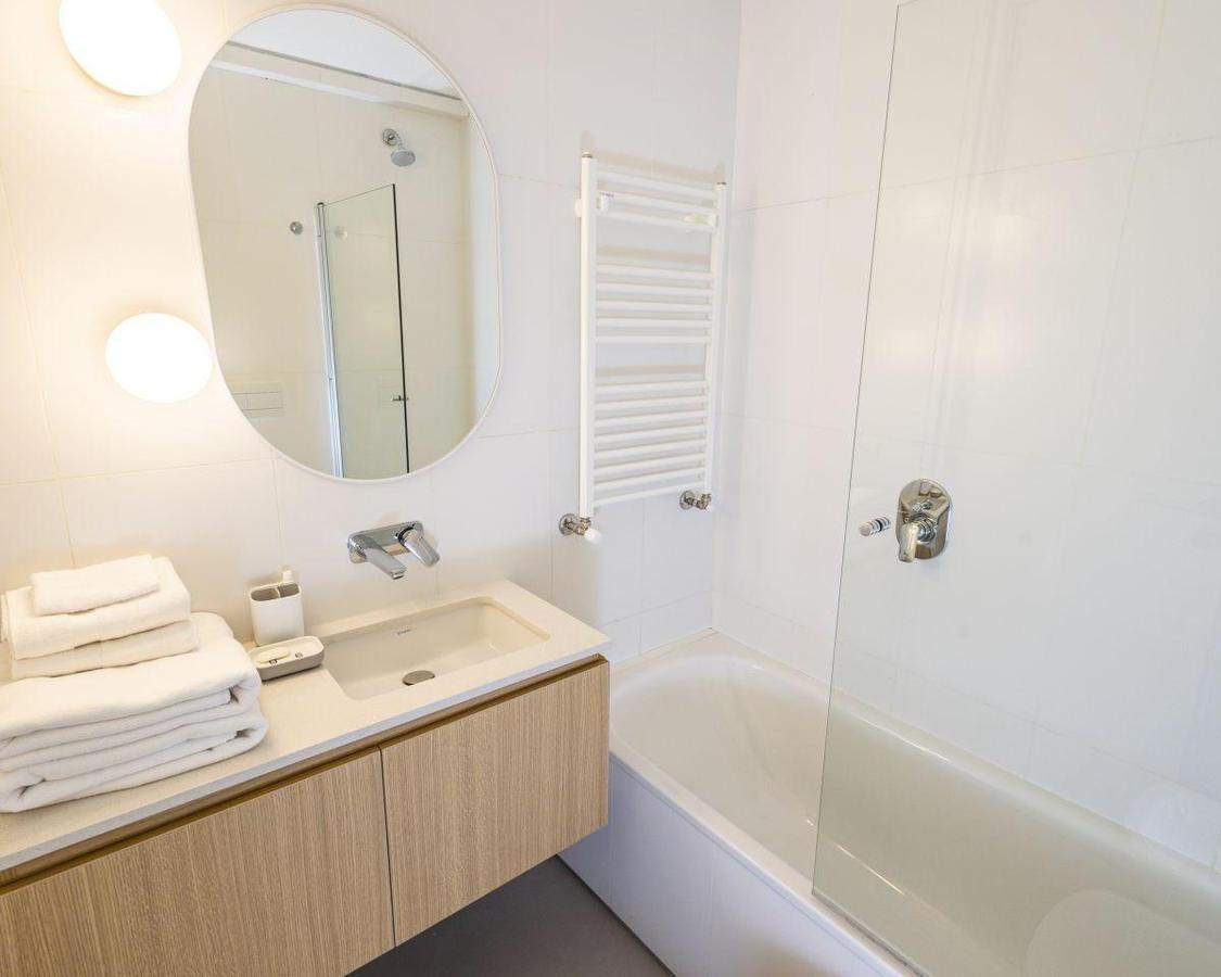 Modern bathroom with a glass-screened bathtub, oval mirror, and folded white towels.
