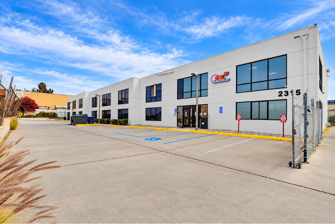 Two-story white commercial building with dark-framed windows, address 2315, and a broad paved parking lot.
