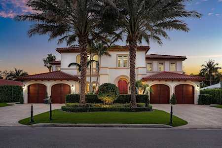 Two-story Mediterranean-style home with arched garages and palm trees at dusk.