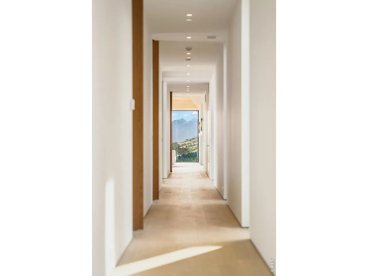 Bright hallway with beige stone floors and a mountain view through the far window.