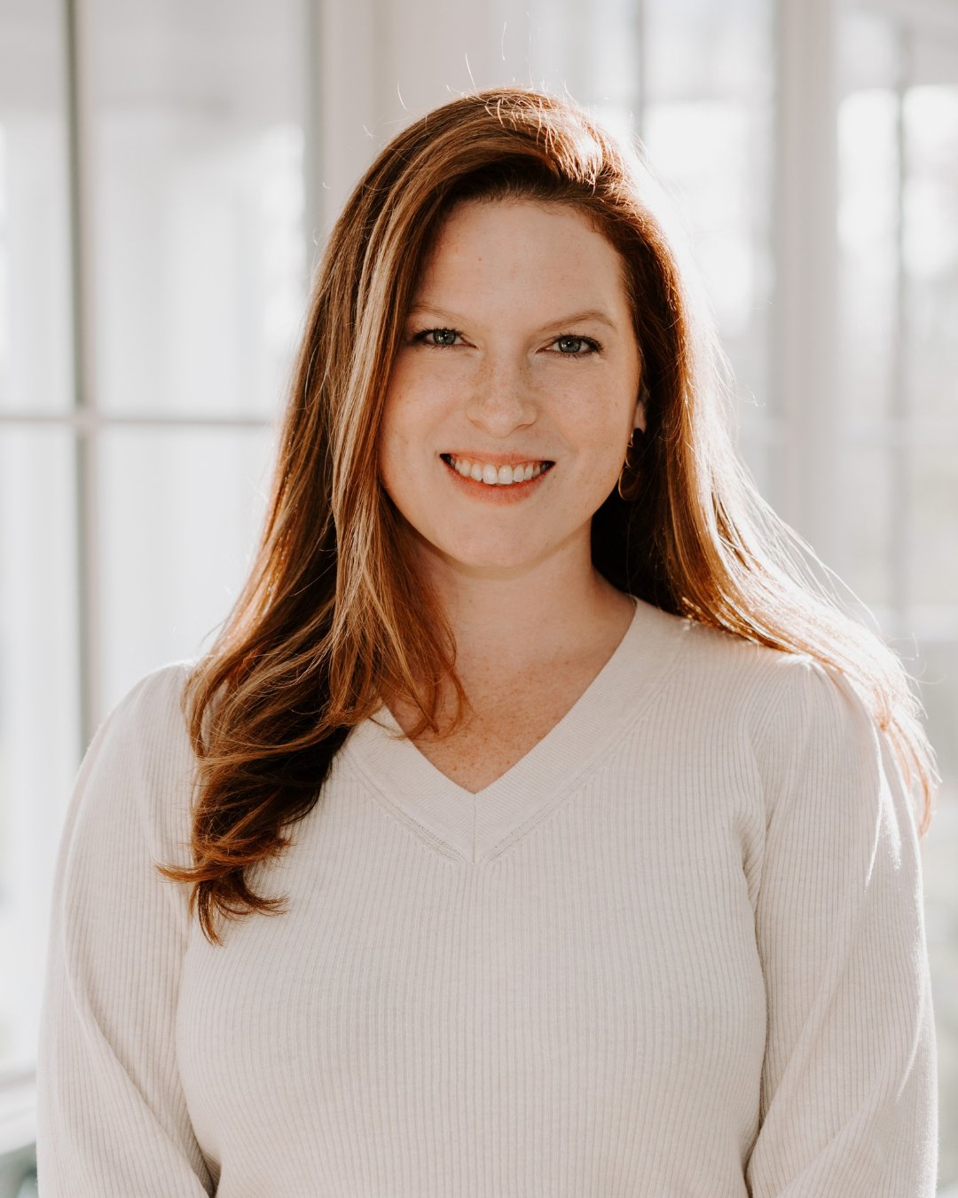 Andrea Ladd smiling in a white sweater against a bright window.