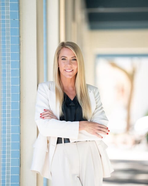 Kristie Barkauskas in a white suit, standing with her arms crossed beside a blue tiled wall.