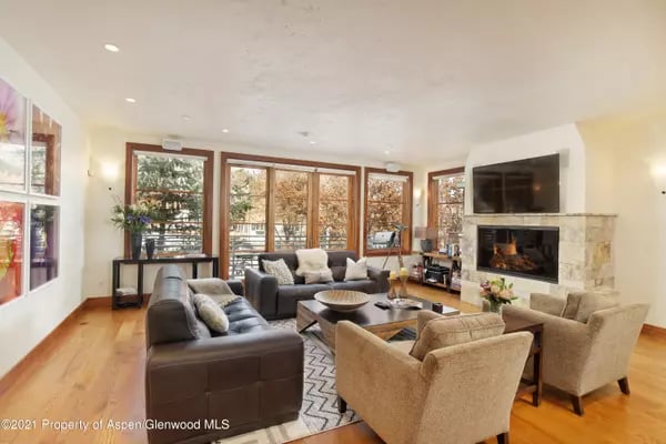 Living room with leather sofas, armchairs, stone fireplace, and large wood-framed windows.