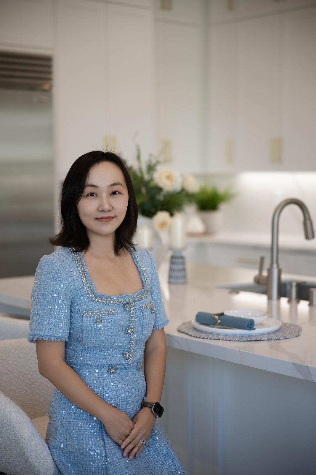 Iris Li in a light blue embellished dress beside a staged kitchen island.