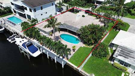 Aerial view of a waterfront home with a curved pool, landscaped yard, and boats at its canal-side dock.