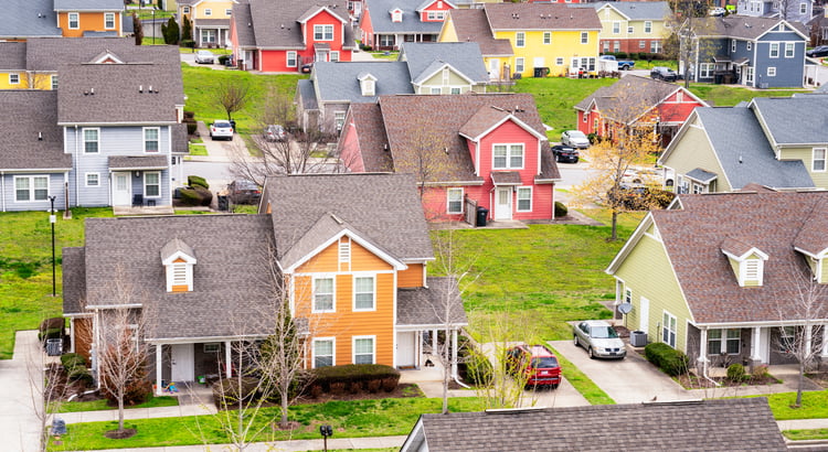 Aerial view of colorful houses in a residential neighborhood with lawns, driveways, and parked cars.