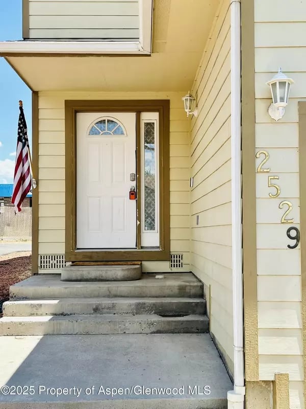 Covered home entrance with a white door, concrete steps, American flag, and house number 2529.