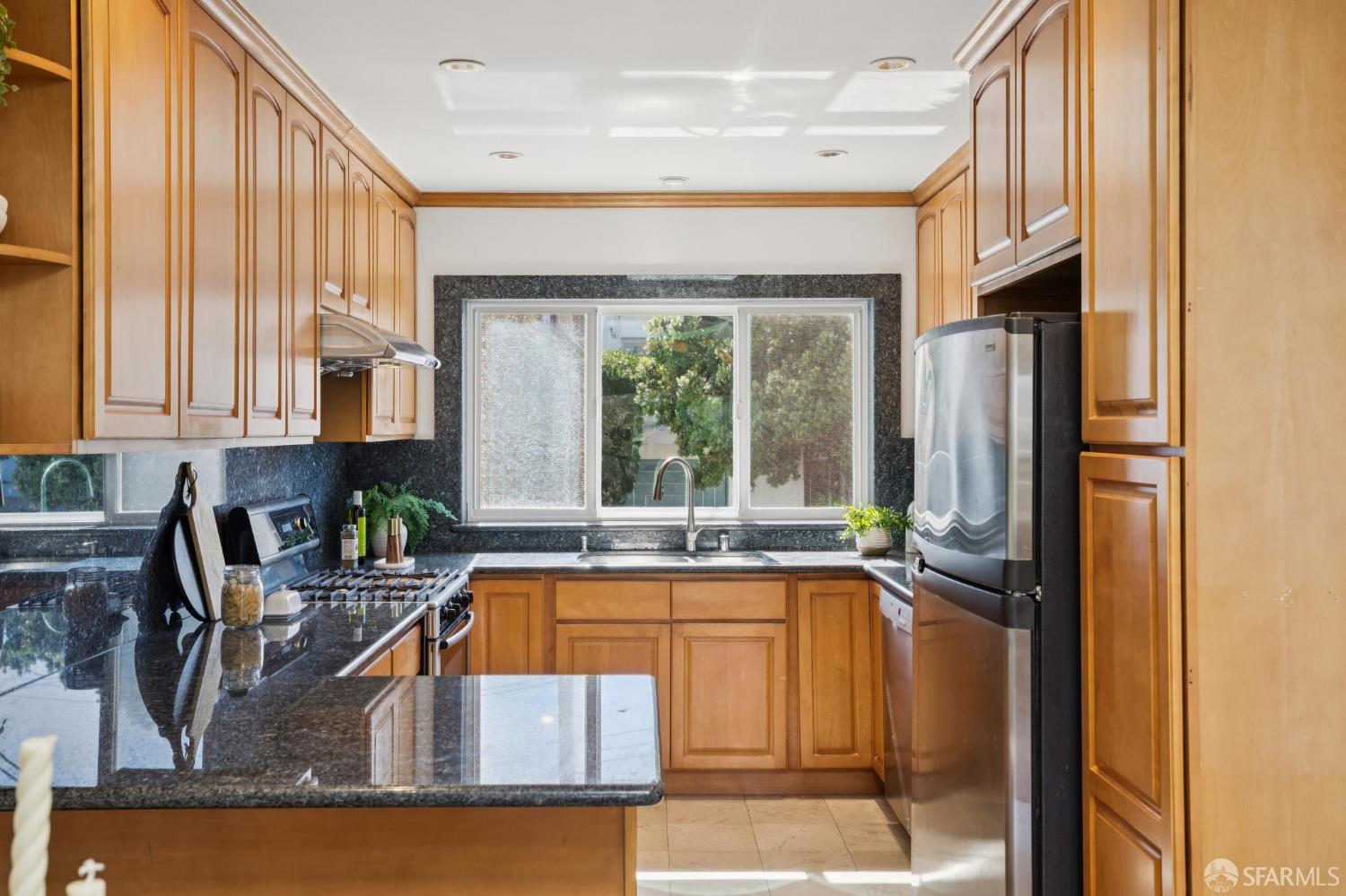 Kitchen with wood cabinets, dark granite countertops, and a sink beneath a wide window.