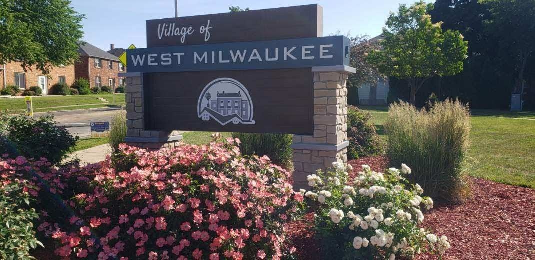 Village of West Milwaukee welcome sign surrounded by flowers and landscaping along a residential street