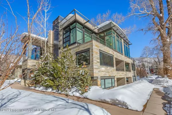 Modern stone-and-glass home with large windows and snow-covered landscaping.