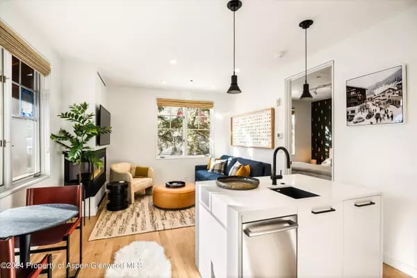 Open-plan kitchen with a white island, black sink, stainless dishwasher, and sunny living area.