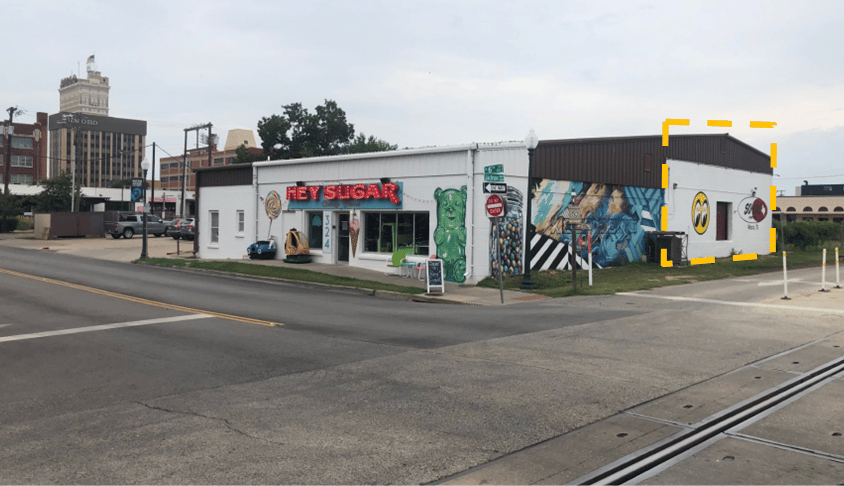 Commercial corner building with colorful murals and a yellow outline highlighting the end section.