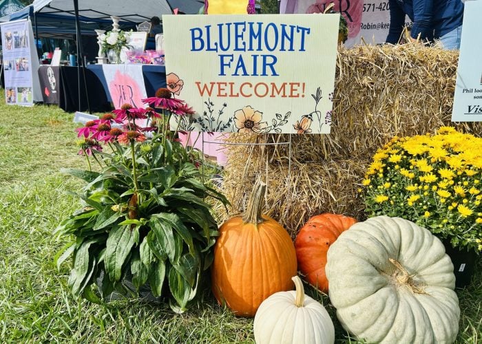 "Bluemont Fair Welcome" sign propped on a hay bale beside pumpkins, yellow mums and pink coneflowers at the fairgrounds in Bluemont, Virginia