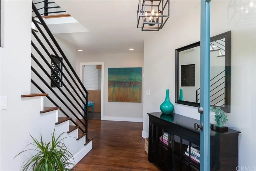  A bright home entryway with dark wood flooring, a modern black staircase railing, and a black console table with a mirror above it.