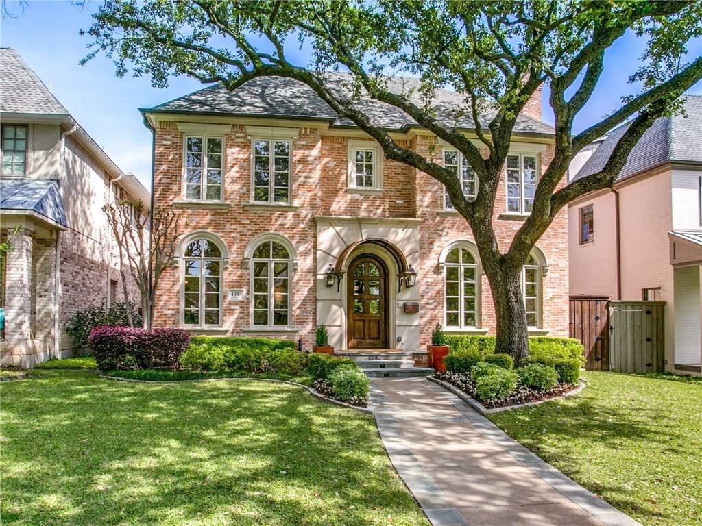 Two-story brick home with arched windows, a large shade tree, and a landscaped front walkway.