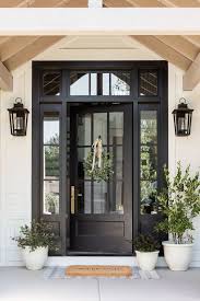 Front entrance with a black glass-paneled door, lantern sconces, and potted plants.