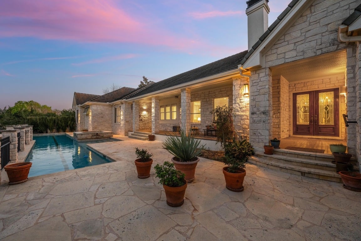 Stone house with a swimming pool and flagstone patio, warmly lit at dusk.