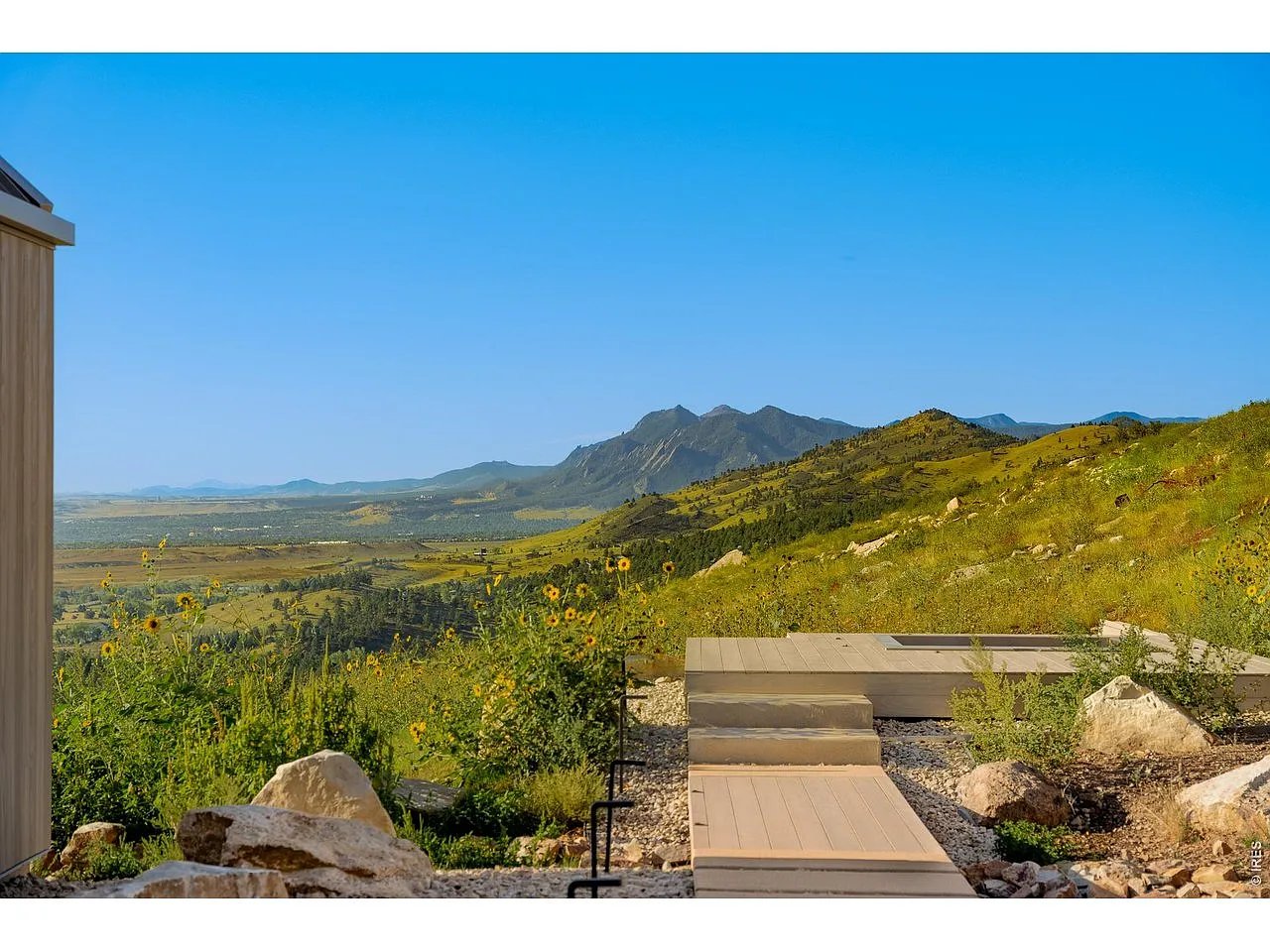 Mountain views from a stone-edged deck with a low wooden platform and wildflowers.