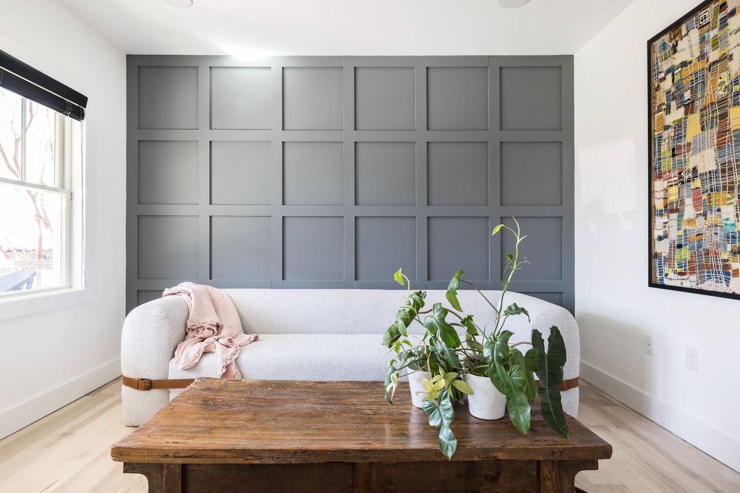 Living room with a gray paneled accent wall, pale sofa, and rustic coffee table with plants.