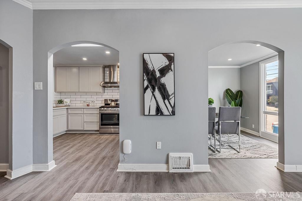 Open interior with arched doorways framing a white kitchen and a dining area beside a large window.