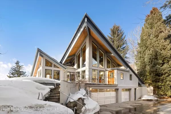 Contemporary A-frame home with large windows and snow-covered front entry.