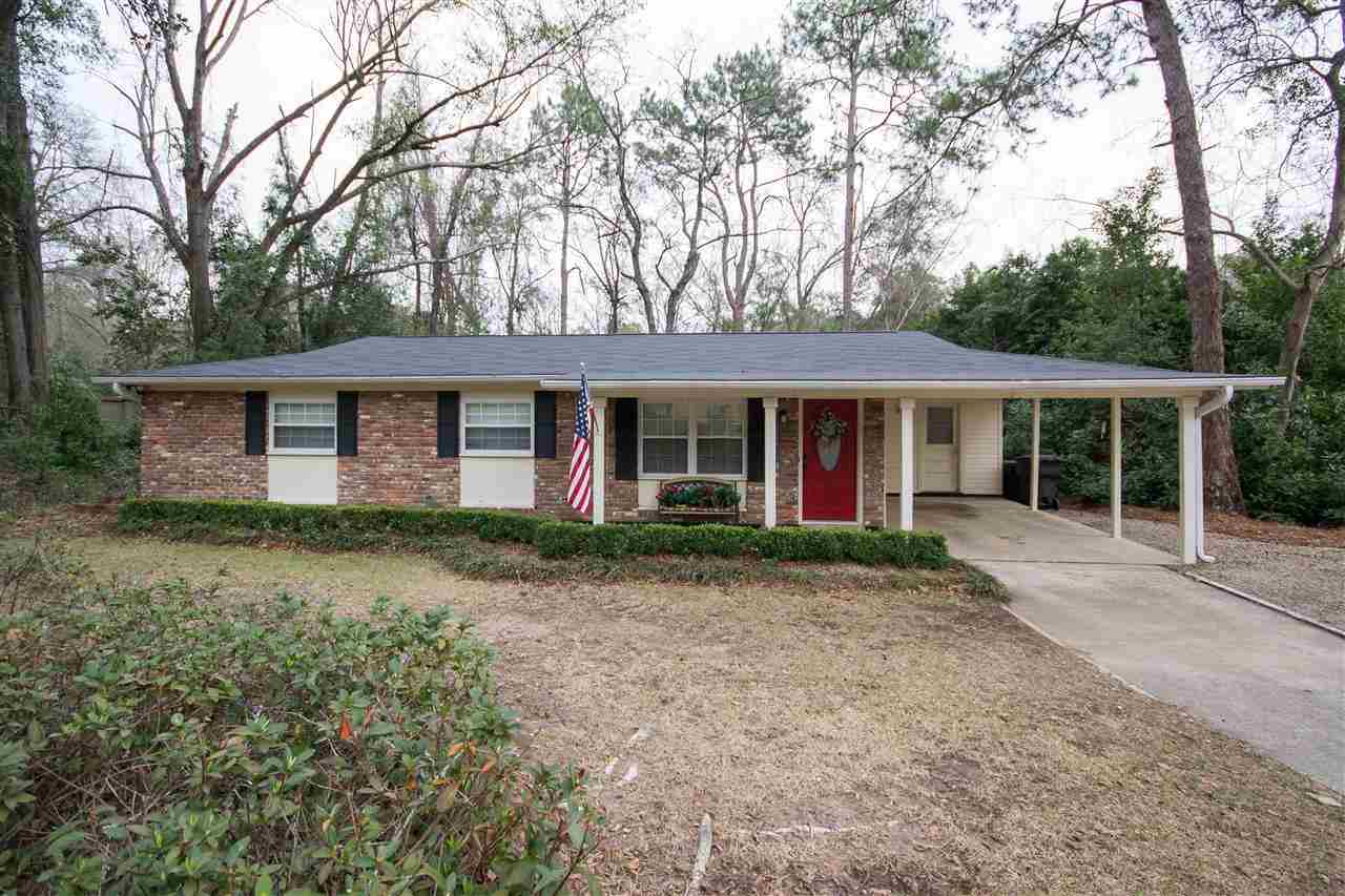 A brick home featuring a vibrant red door, surrounded by a well-maintained front yard.