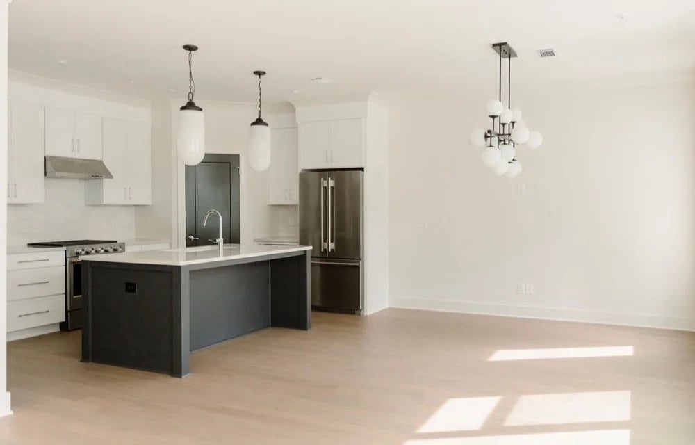 Vacant condo kitchen with a dark island, stainless steel appliances, and an open dining area.