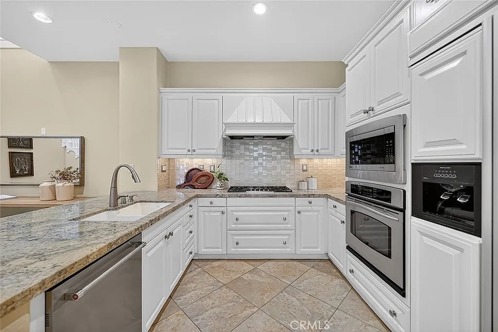 Kitchen with white cabinetry, granite counters, a tiled backsplash, and built-in microwave and oven.
