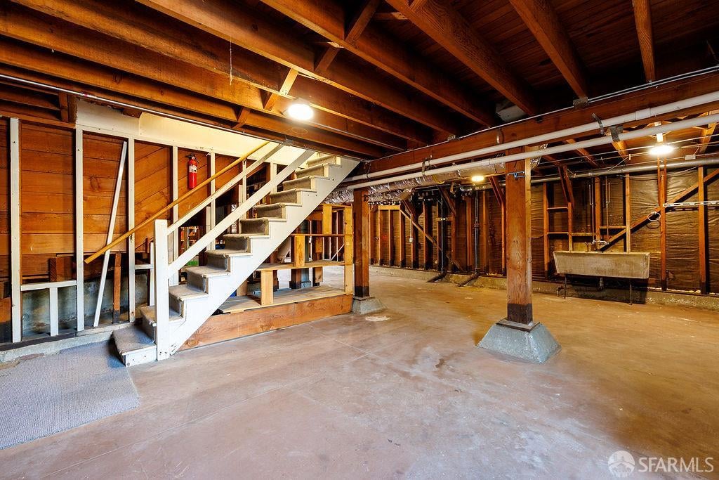 Unfinished basement with exposed wood framing, concrete floor, and an open staircase.