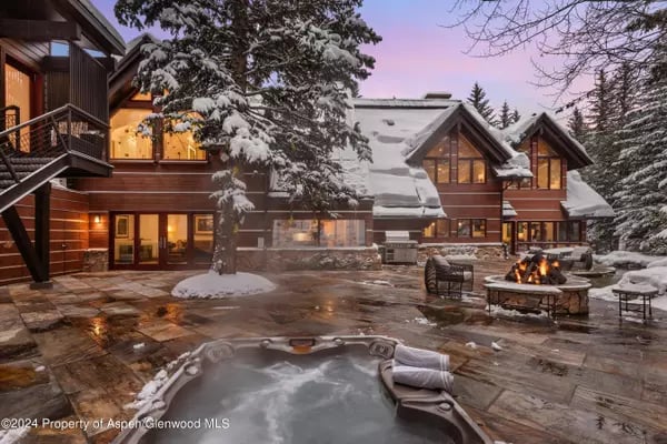 Snowy mountain home with a bubbling hot tub and patio fire pit at dusk.