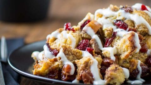 Bowl of chunky breakfast granola with dried cranberries, nuts, and a yogurt drizzle.