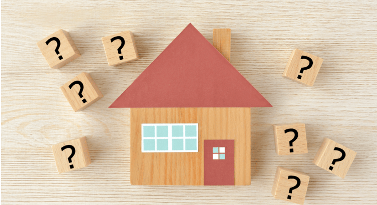 Wooden model house surrounded by blocks marked with question marks.