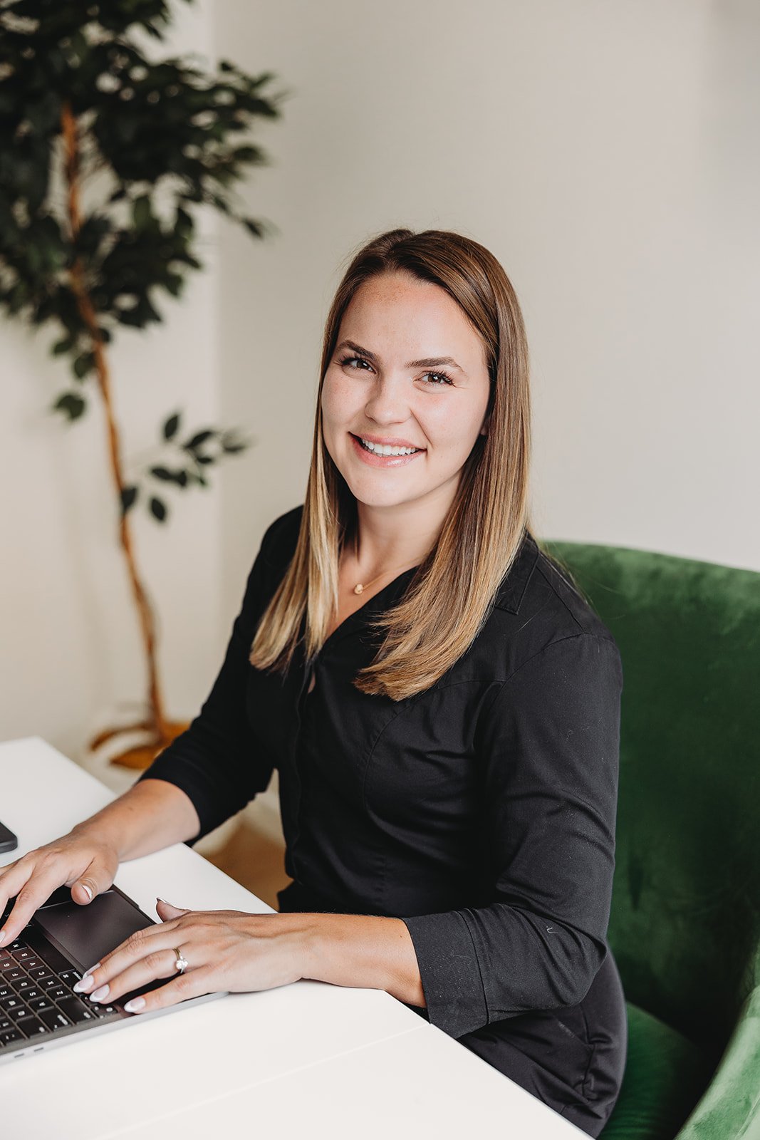 Woman in a black blouse smiling at a desk with a laptop
