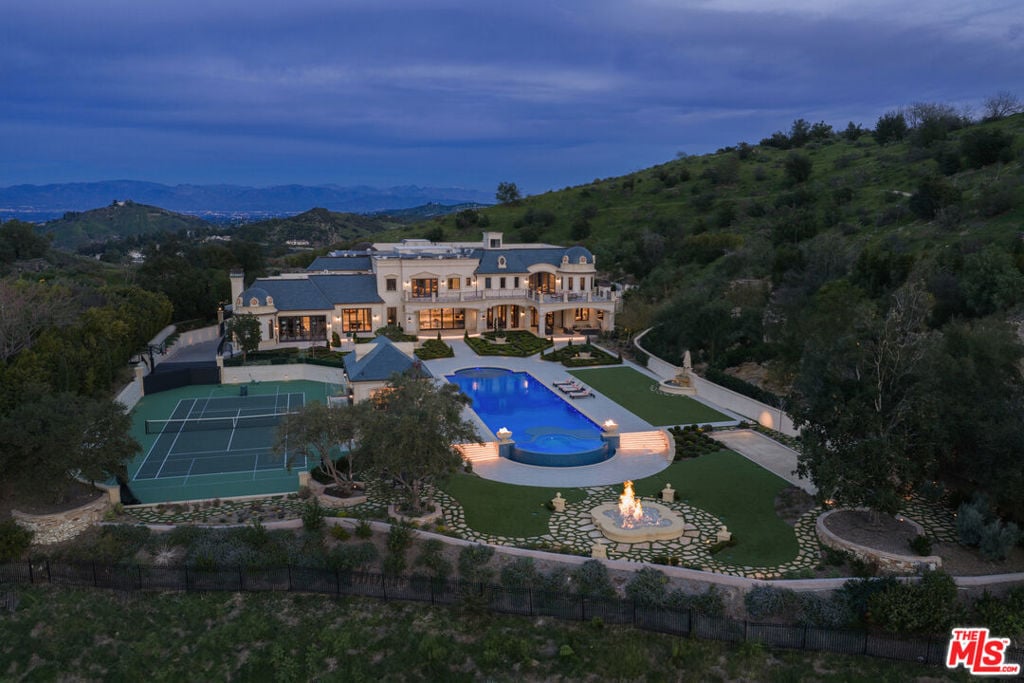 Hillside estate with a blue swimming pool, tennis court, and landscaped grounds at dusk.