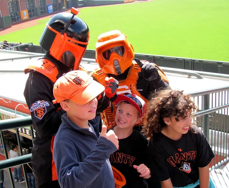 Children posing with Star Wars characters in custom orange and black Mandalorian armor at Oracle Park during the San Francisco Giants Star Wars Day event.