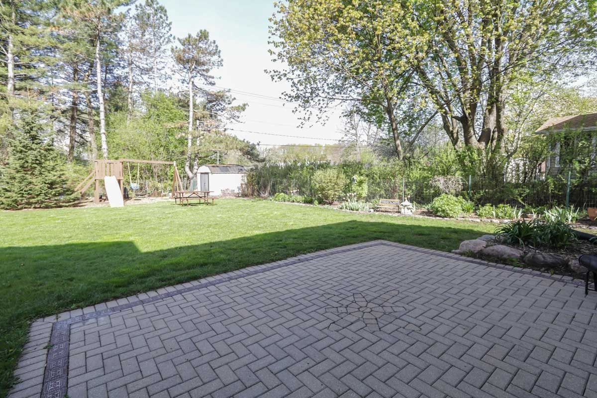 Backyard with a wide paver patio, green lawn, swing set, and mature trees.