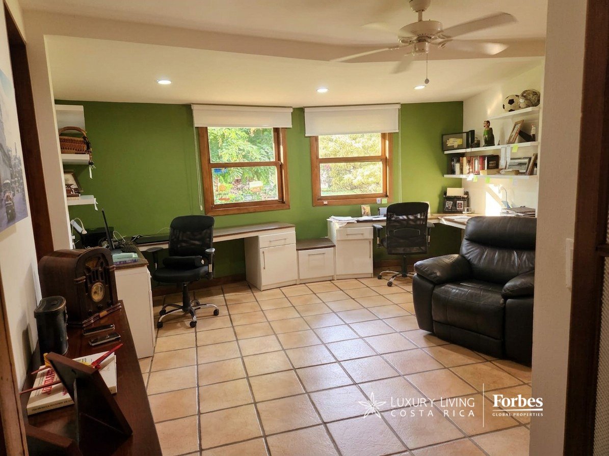 Home office with green walls, built-in desks, tiled floors, and a black leather recliner.
