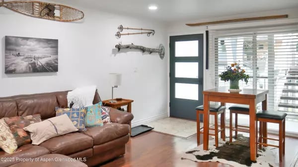Living and dining area with a brown leather sectional, colorful pillows, and a wooden table by wide windows.