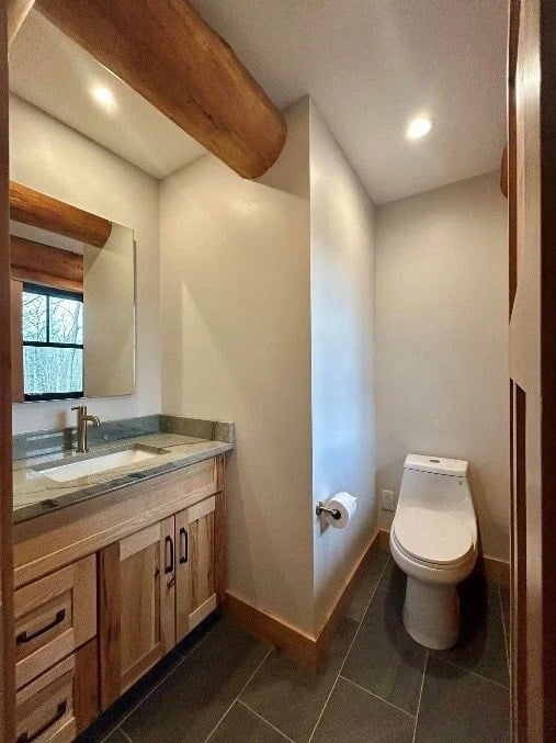 Bathroom with a wood vanity and separate toilet alcove beneath an exposed log beam.