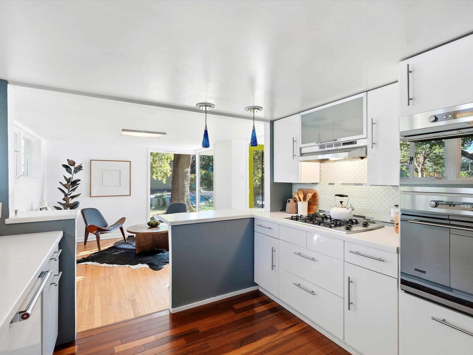 Bright modern kitchen with white cabinets, stainless appliances, gas cooktop, and a peninsula opening to a sitting area.