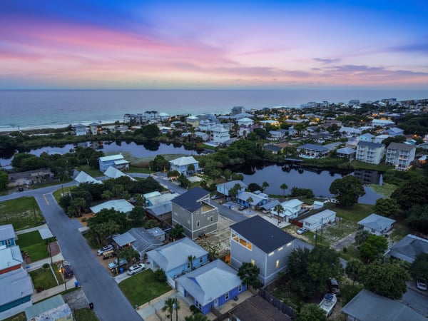 Coastal neighborhood at dusk, with homes around a lagoon and the ocean beyond.