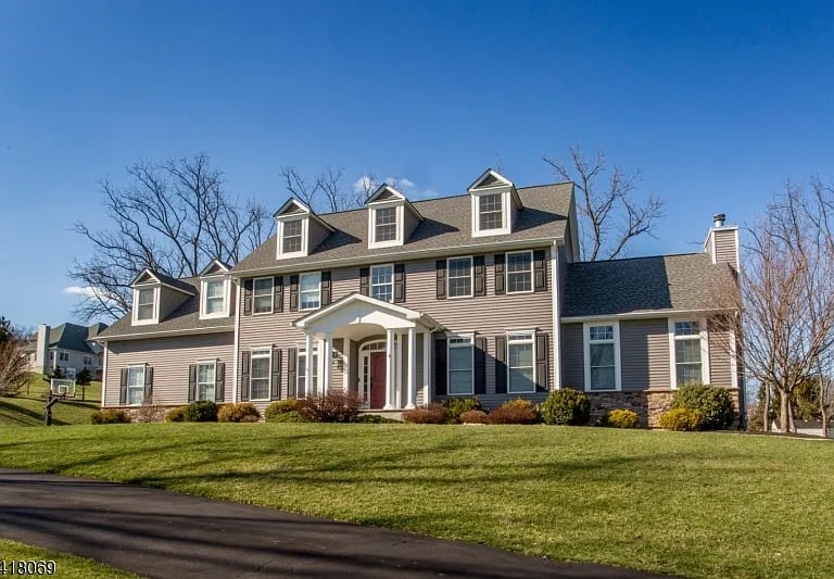 Two-story taupe home with multiple dormers, white columned entry, and broad front lawn.