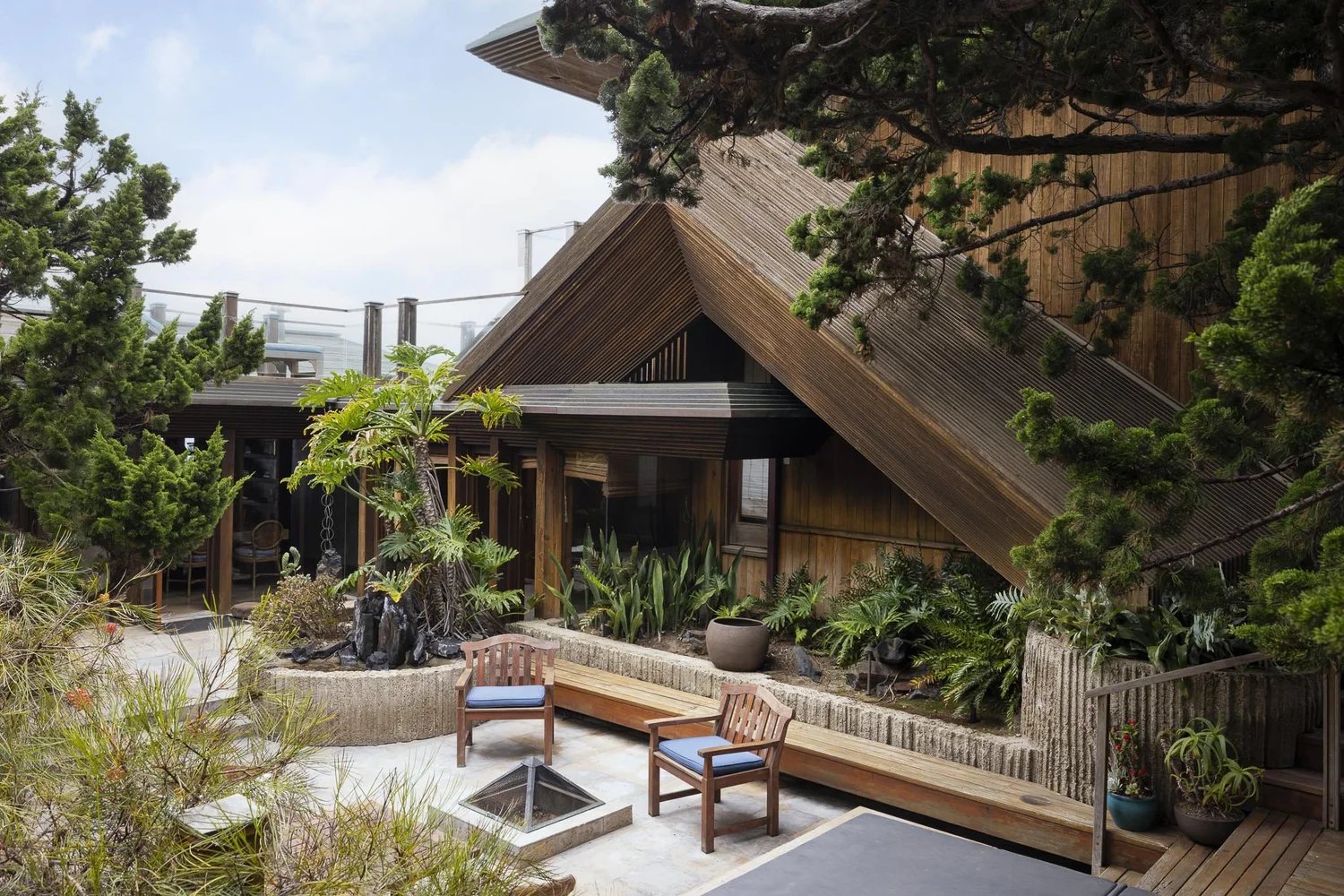 Courtyard of the Kravis Residence with concrete planters, low garden walls, built-in bench seating, and the angled wood roofline above.