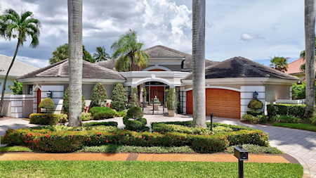 Home with an arched entry, attached garage, palm trees, and landscaped front garden.