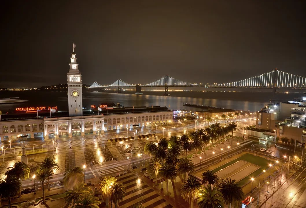 San Francisco Ferry Building and Bay Bridge at night with the red Port of San Francisco neon sign.