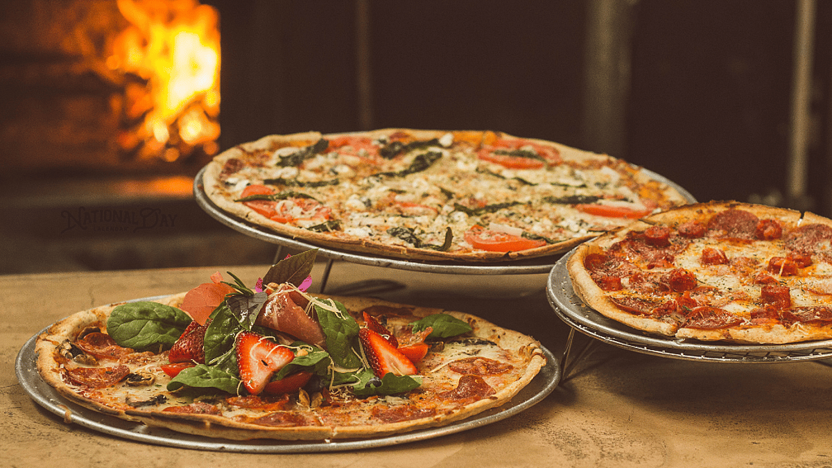 Three pizzas on trays, including pepperoni and tomato-herb varieties, with greens and strawberries on the foreground pizza.