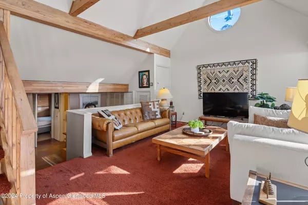 Living room with exposed timber beams, a tan leather sofa, and red carpet.