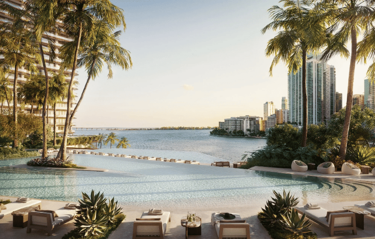 Waterfront pool deck with palm trees, lounge chairs, and Miami high-rises across the bay.