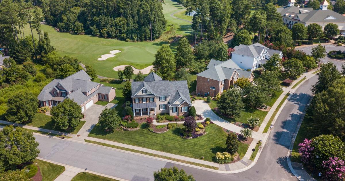 Aerial view of a residential golf community, with homes and landscaped yards along a fairway lined with pine trees.